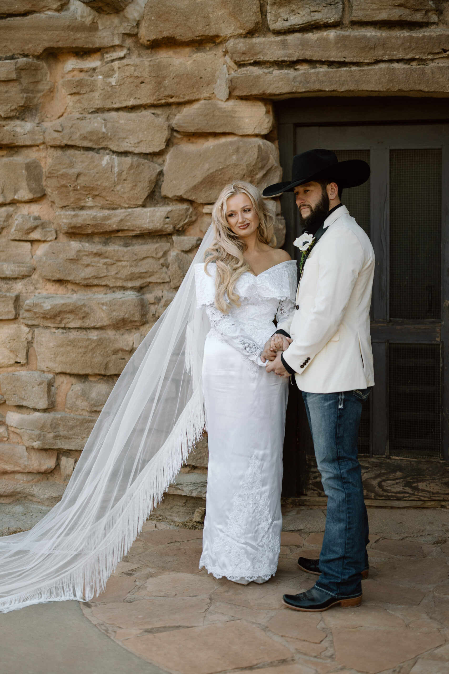 Bride in a fringe cathedral veil and groom in a white tuxedo jacket at Palo Duro Canyon State Park.