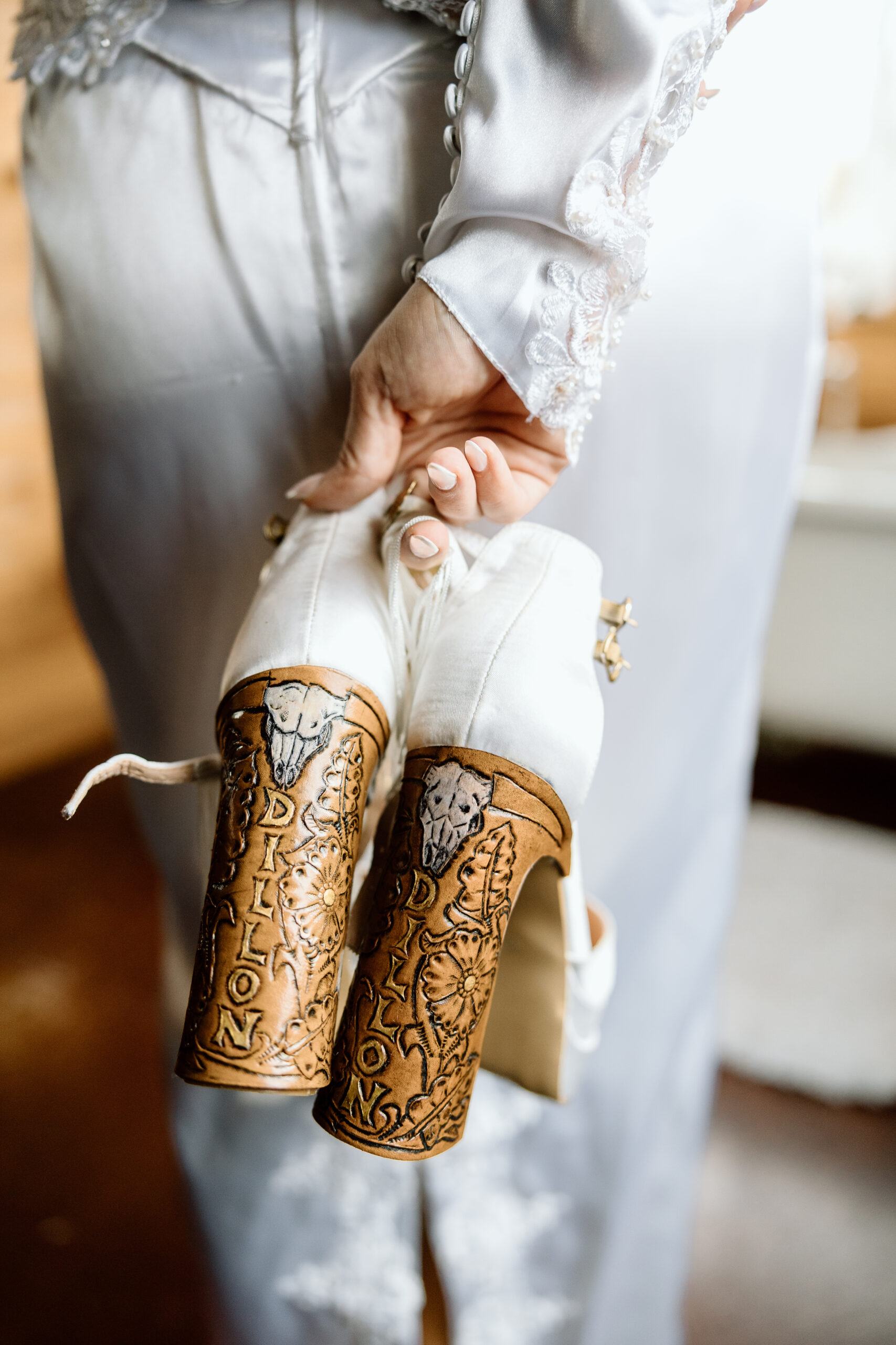 White Western elopement heels with fringe and custom engraved wood-tooled heel details.