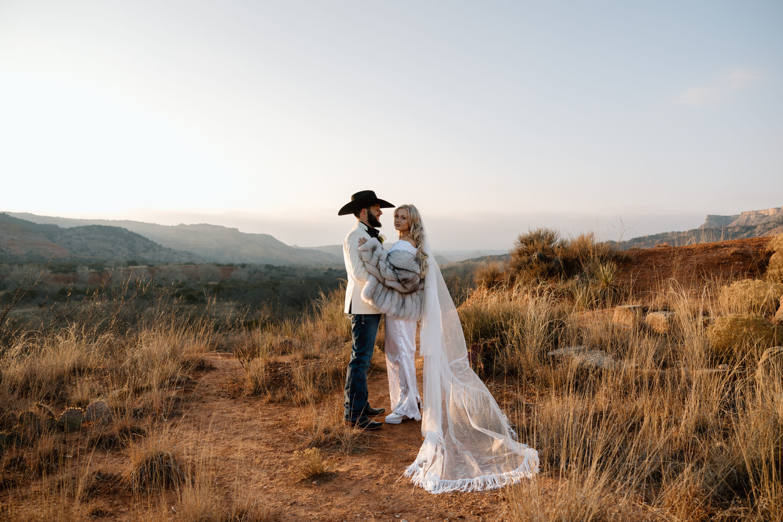 Epic wide-angle elopement photo of a couple standing on the red rocks of Palo Duro Canyon at golden hour.