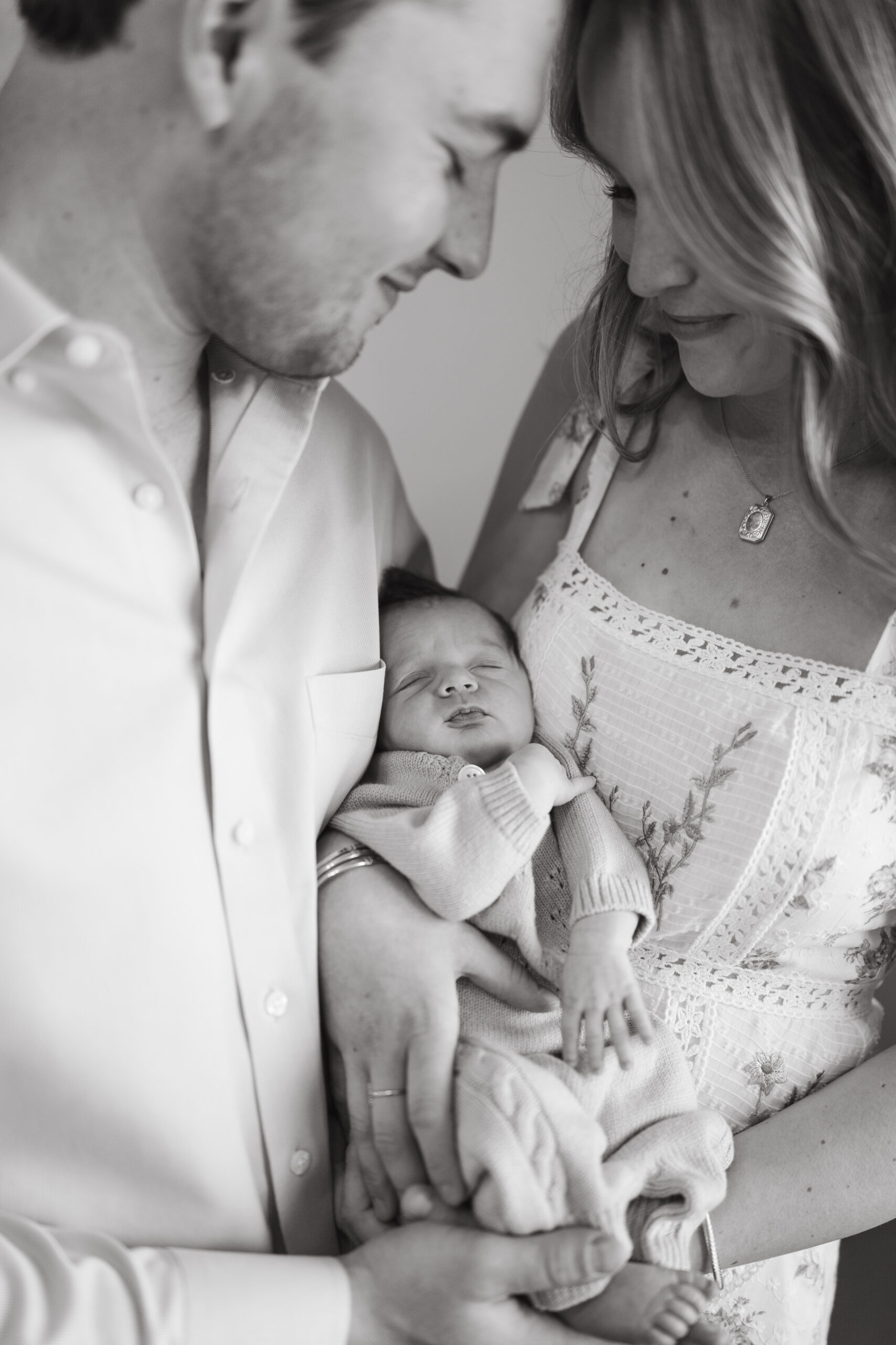 Parents cuddle their new baby during an intimate in-home photo session, featuring our lifestyle newborn photography tips.