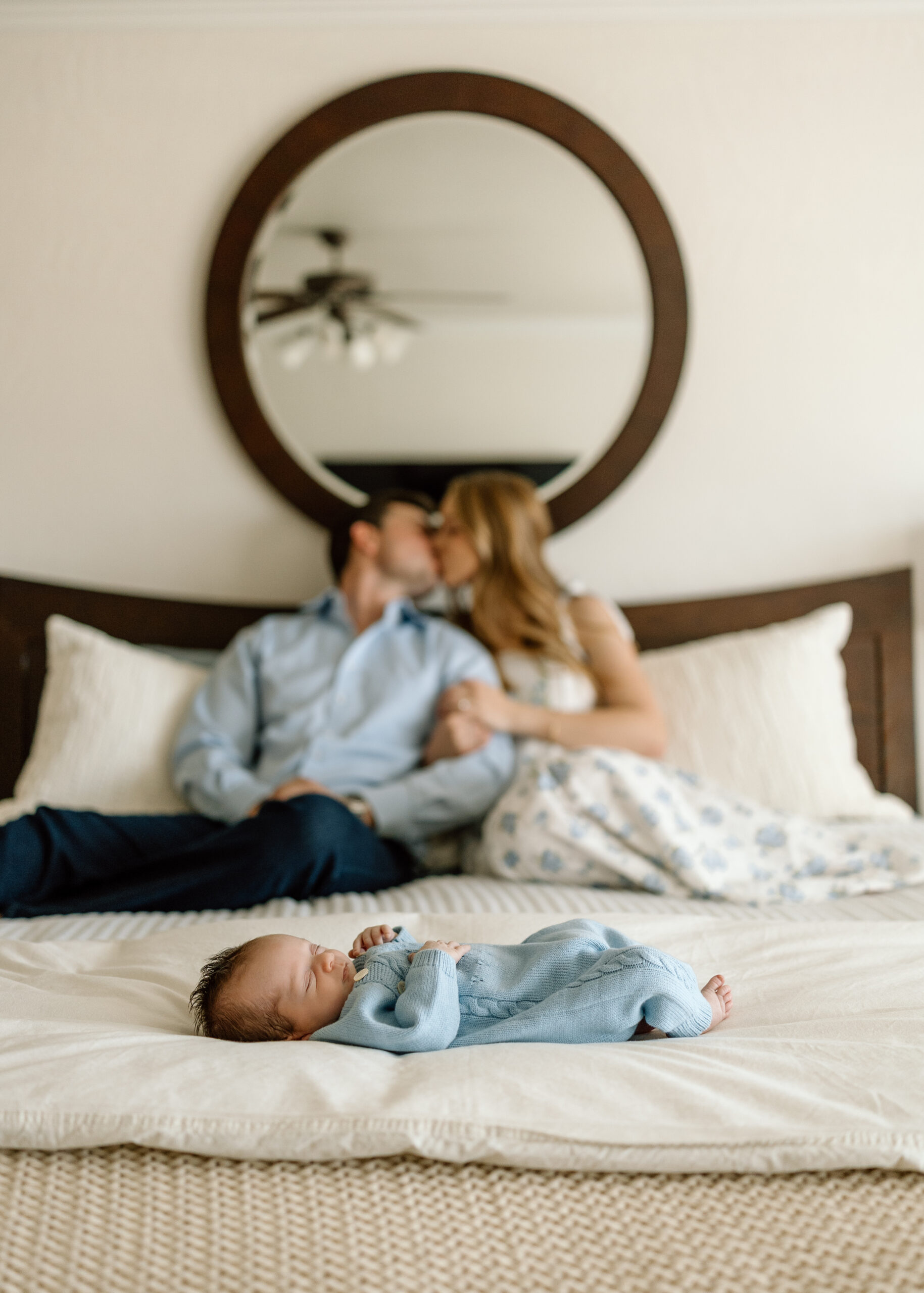 A happy family posing on their bed with their new baby boy, showcasing our natural newborn photos at home tips.