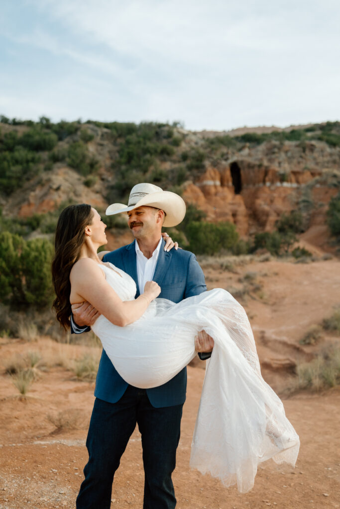 Bride in flowing white dress with cowboy-hat groom in Palo Duro Canyon