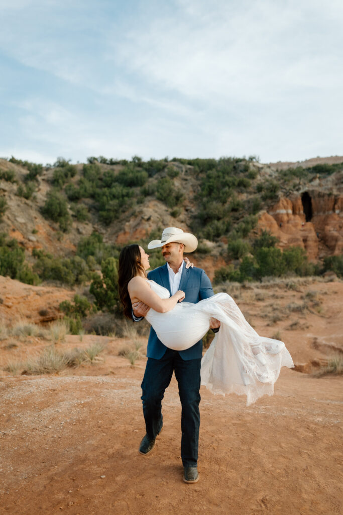 Bride in flowing white dress with cowboy-hat groom in Palo Duro Canyon